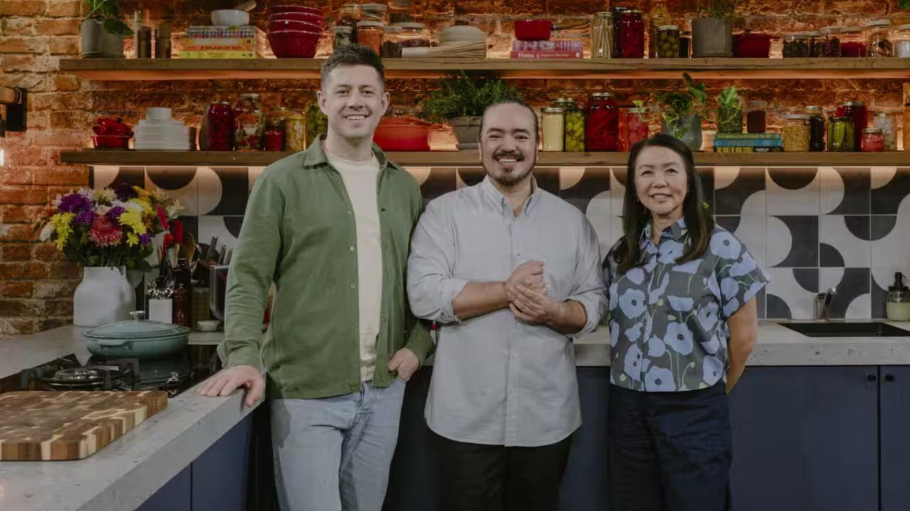Three people smiling in a modern kitchen with shelves of jars