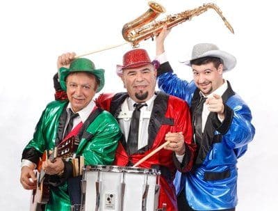 Three musicians in green, red, and blue jackets holding instruments and posing together