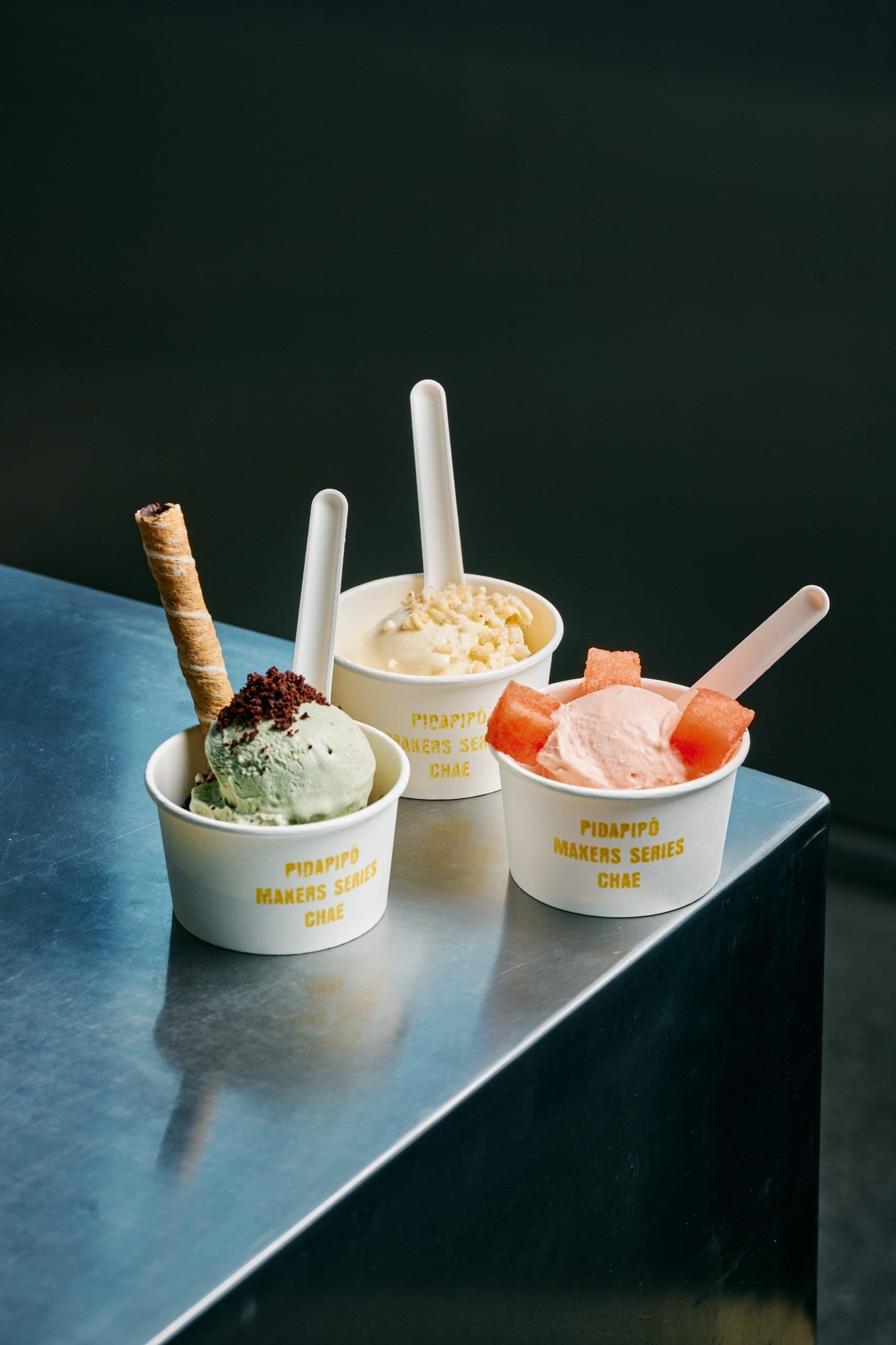 Three gelato cups with pistachio, coconut, and watermelon flavours on counter