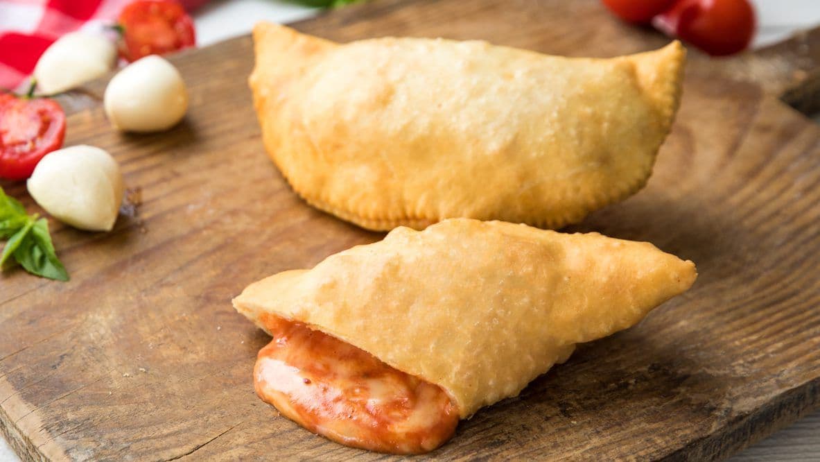 Golden fried panzerotti on wooden board with cherry tomatoes and mozzarella