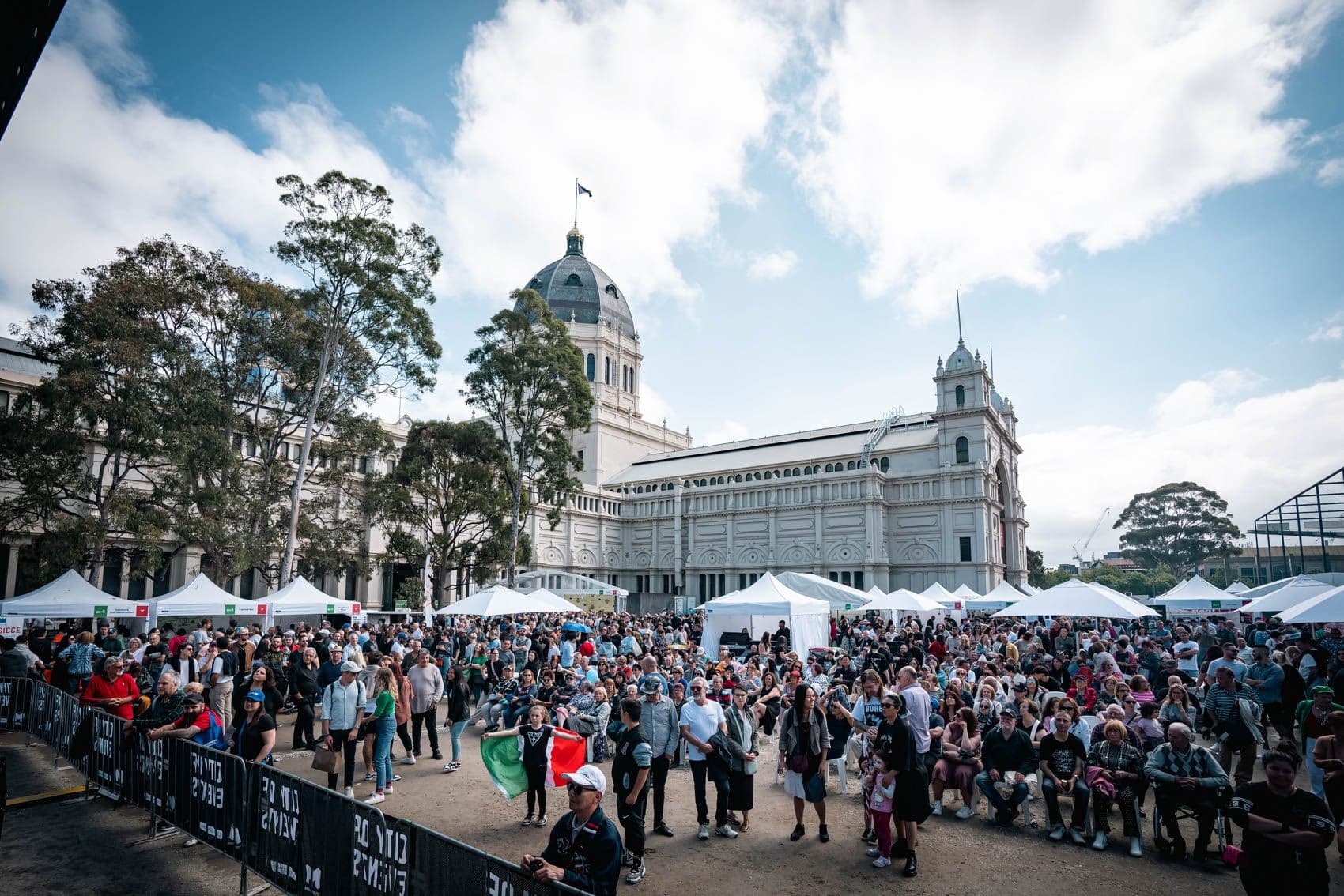 Large crowd gathering at Melbourne Italian Festa with white tents, historic building backdrop
