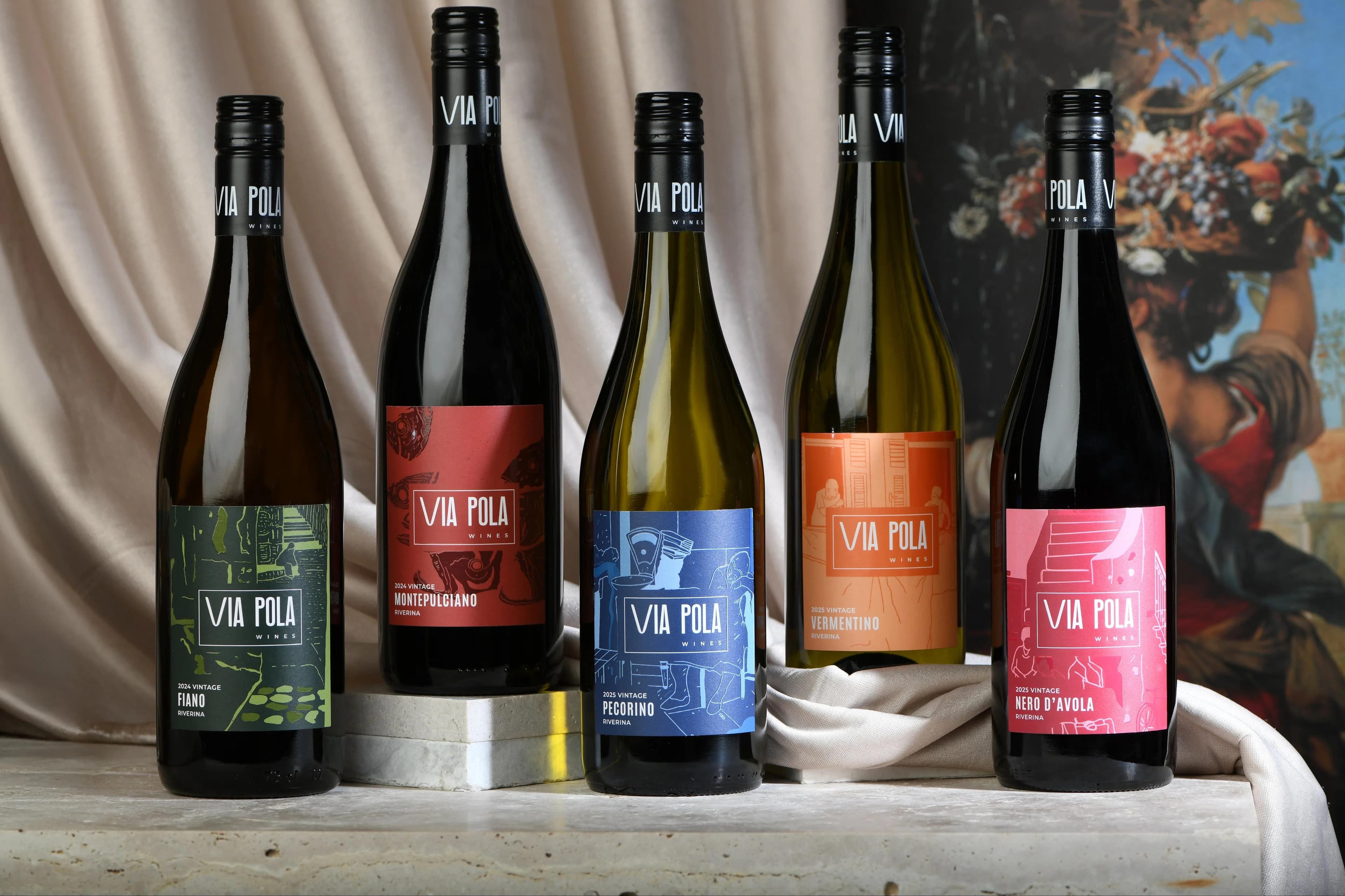 Five Via Pola wine bottles lined up with colourful labels