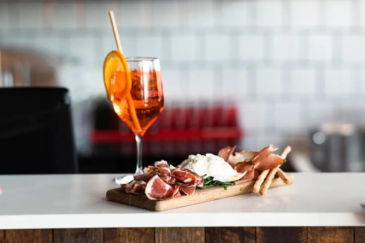 Aperol spritz beside charcuterie board with prosciutto and burrata