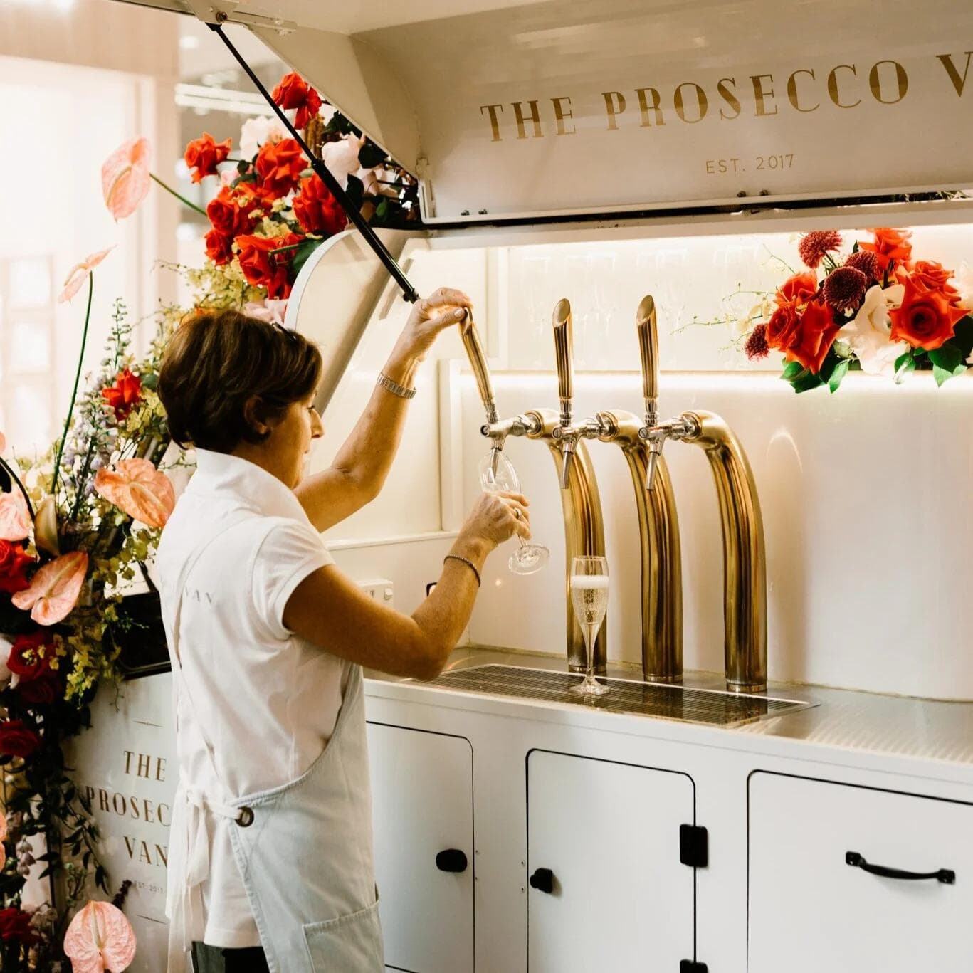 Person pouring prosecco from gold taps on floral-decorated van