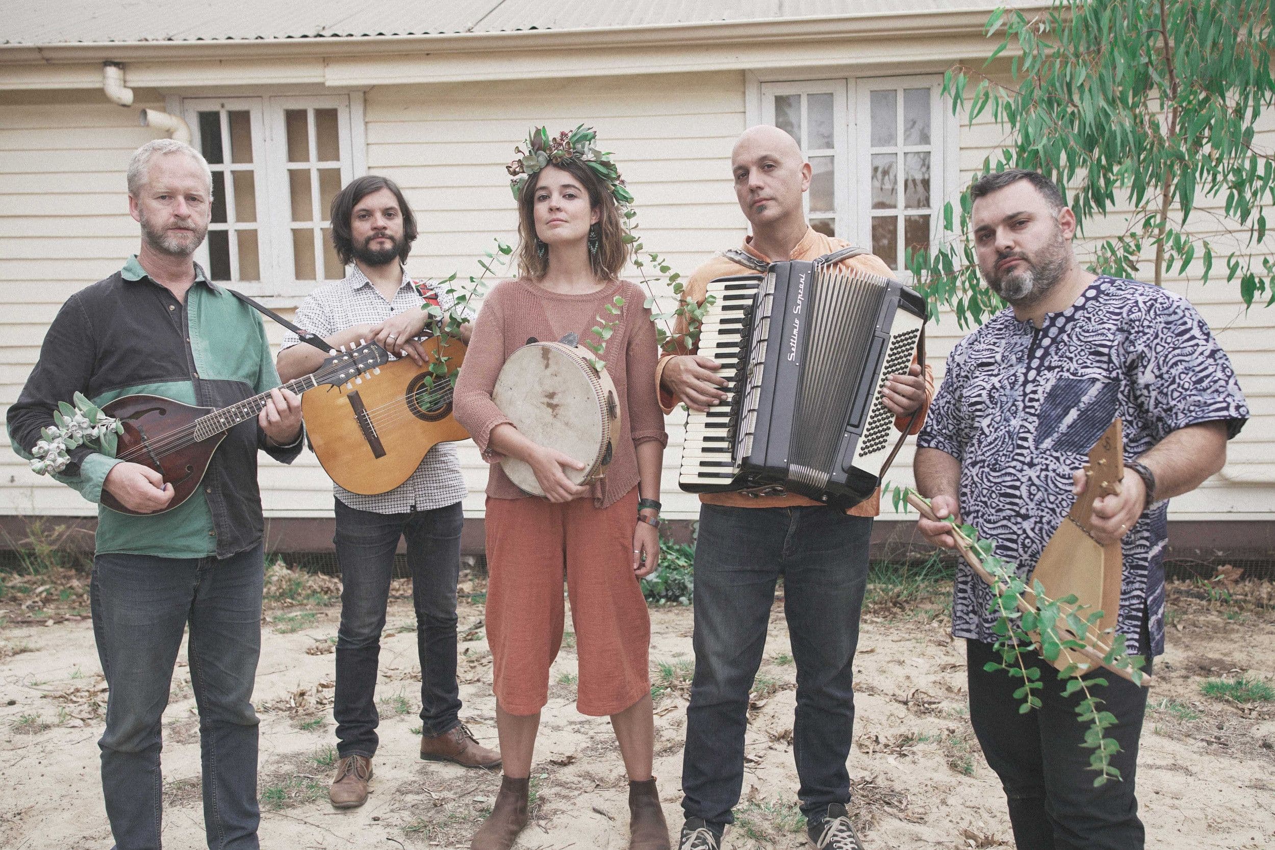 Five musicians holding traditional Italian folk instruments, wearing floral garlands outdoors
