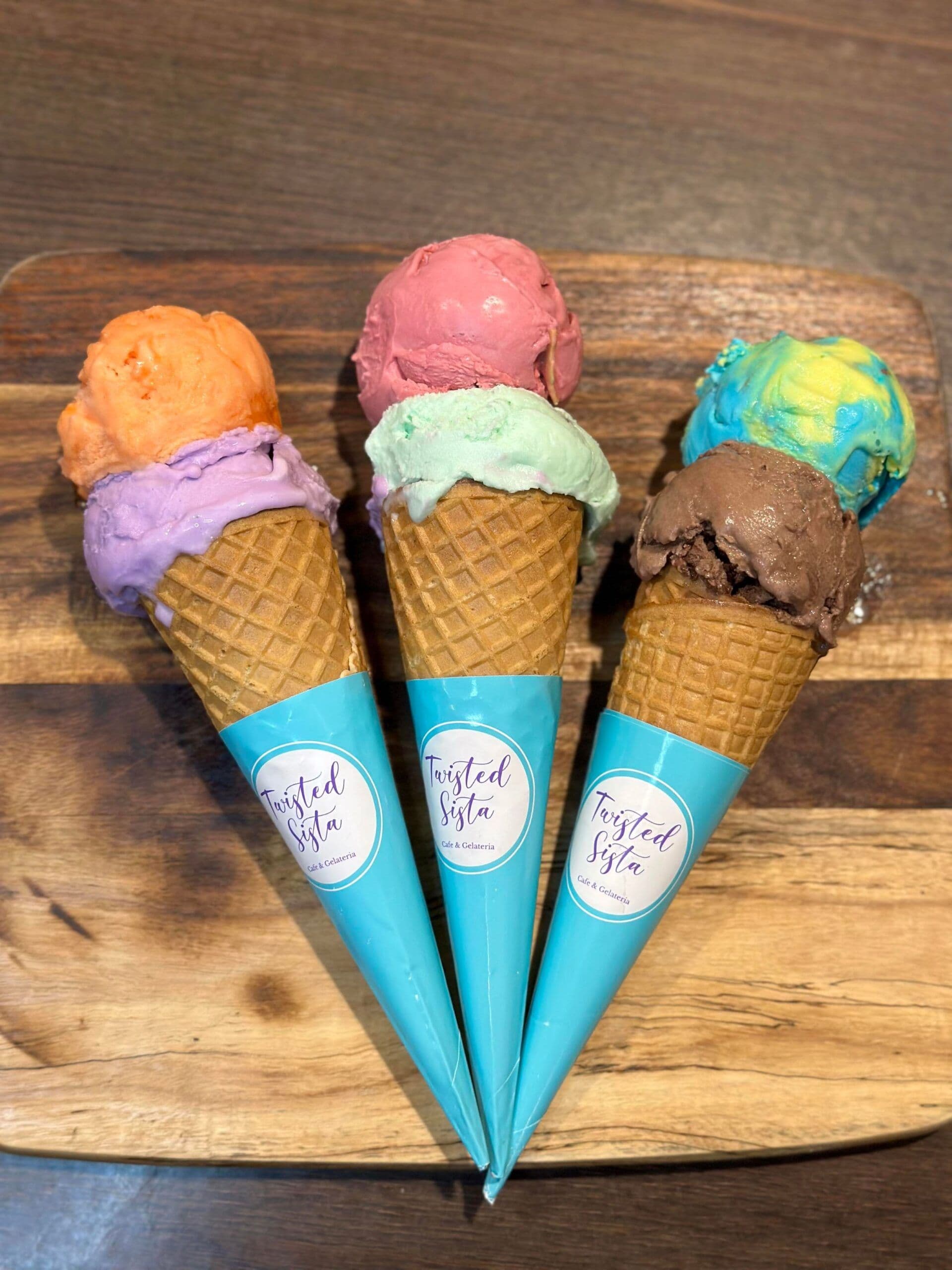 Three waffle cones with colourful gelato scoops on wooden board