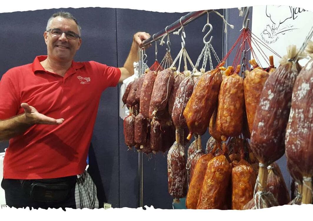 Vendor smiling beside rows of hanging cured salami at stall