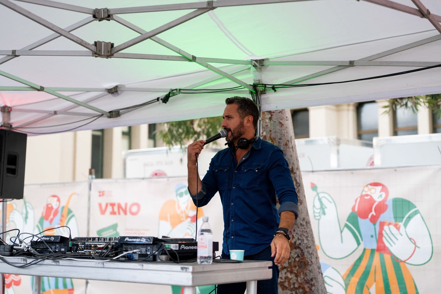 DJ performing at microphone under tent with Pioneer equipment at Melbourne Italian Festa