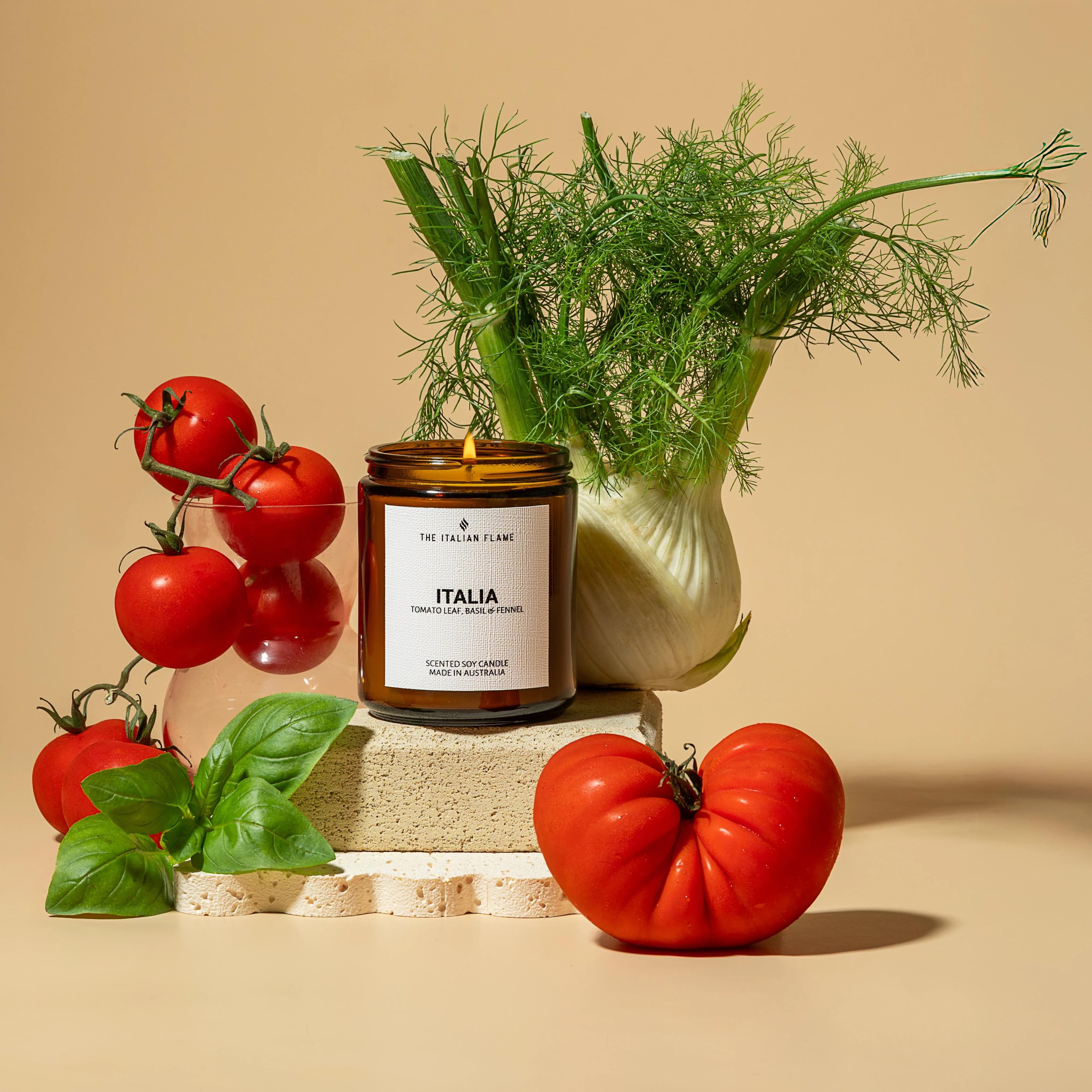Lit amber candle jar surrounded by tomatoes, basil and fennel