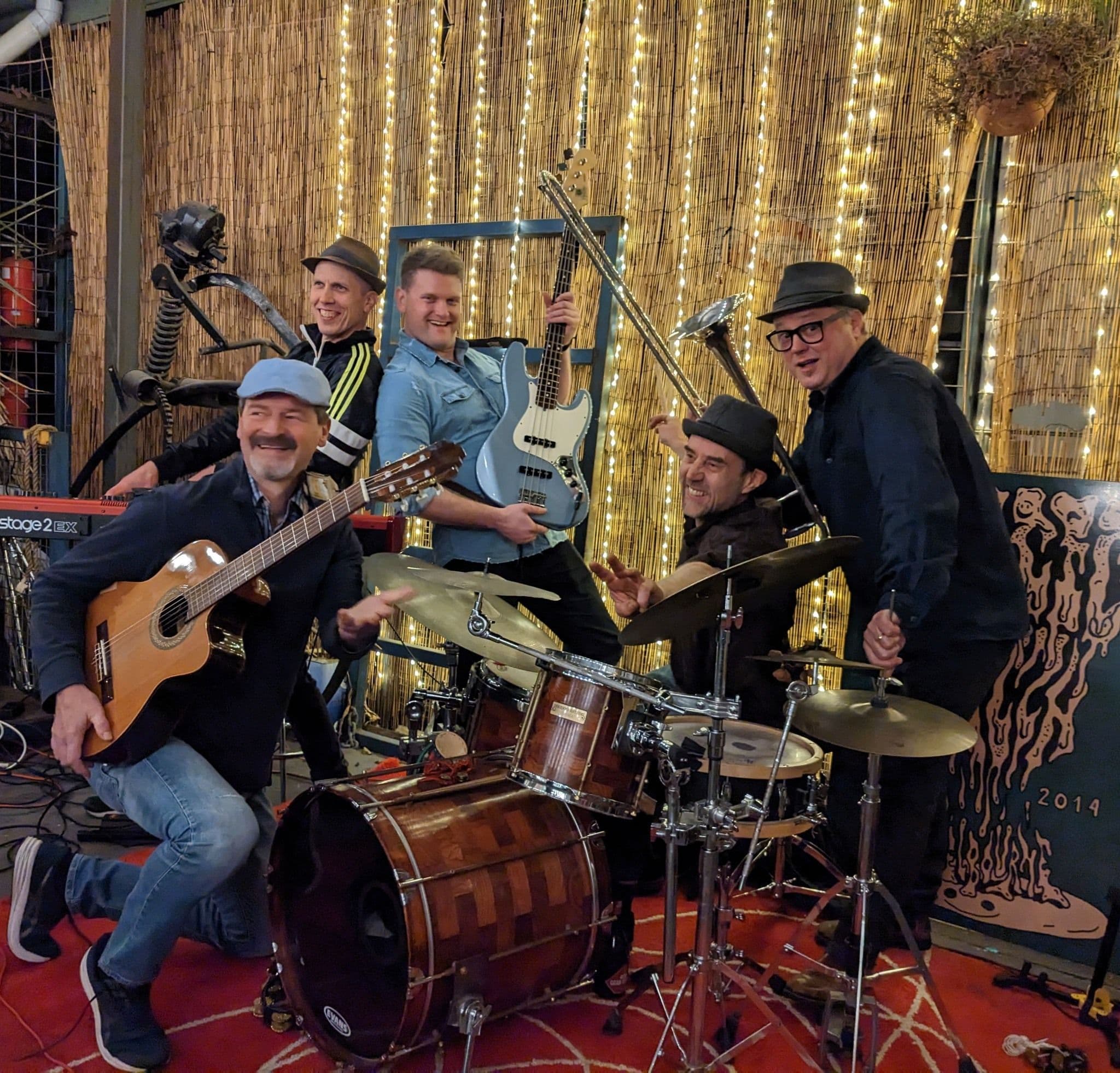 Five musicians with guitars, bass, and drums performing against illuminated backdrop