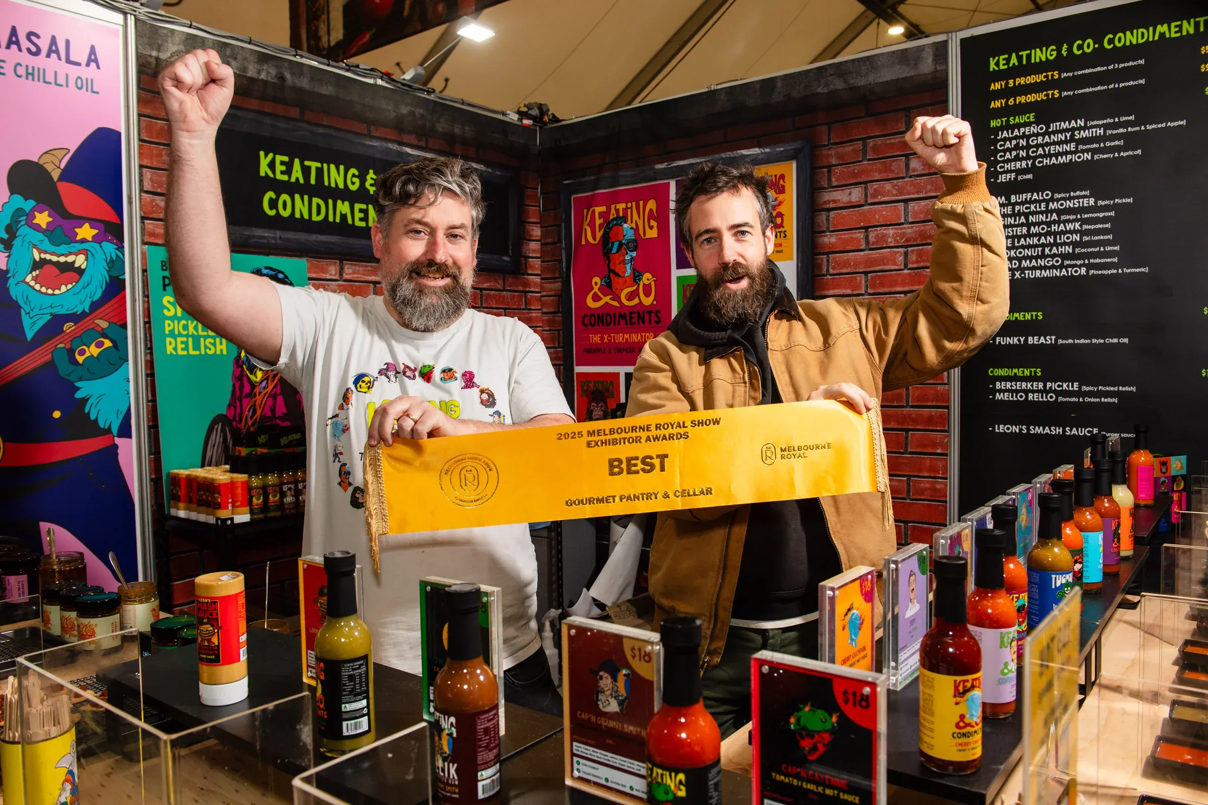 Two men holding award ribbon behind stall of hot sauce bottles
