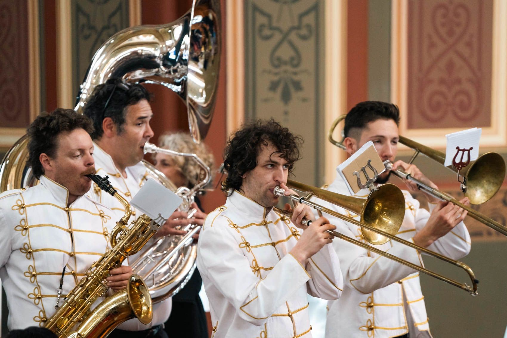 Brass band musicians in white and gold uniforms performing in ornate hall