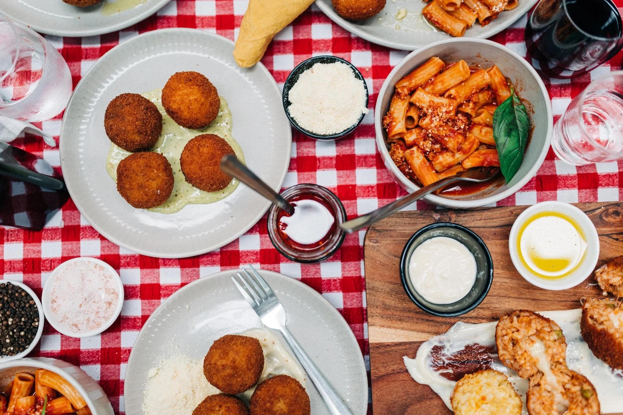 Arancini balls, pasta, and dips on checkered tablecloth spread