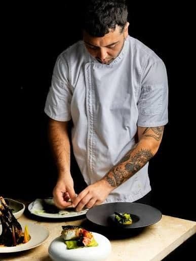 Akela Nevelli plating dishes at a work station against a black background