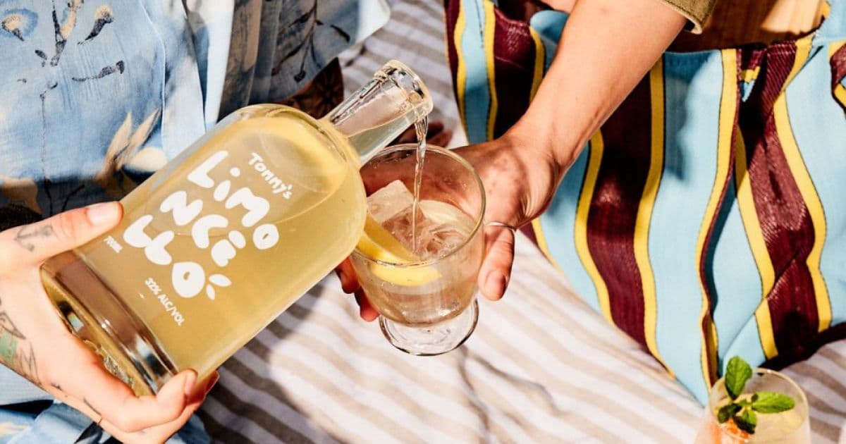 Hands pouring Tommy's limoncello bottle into glass with ice