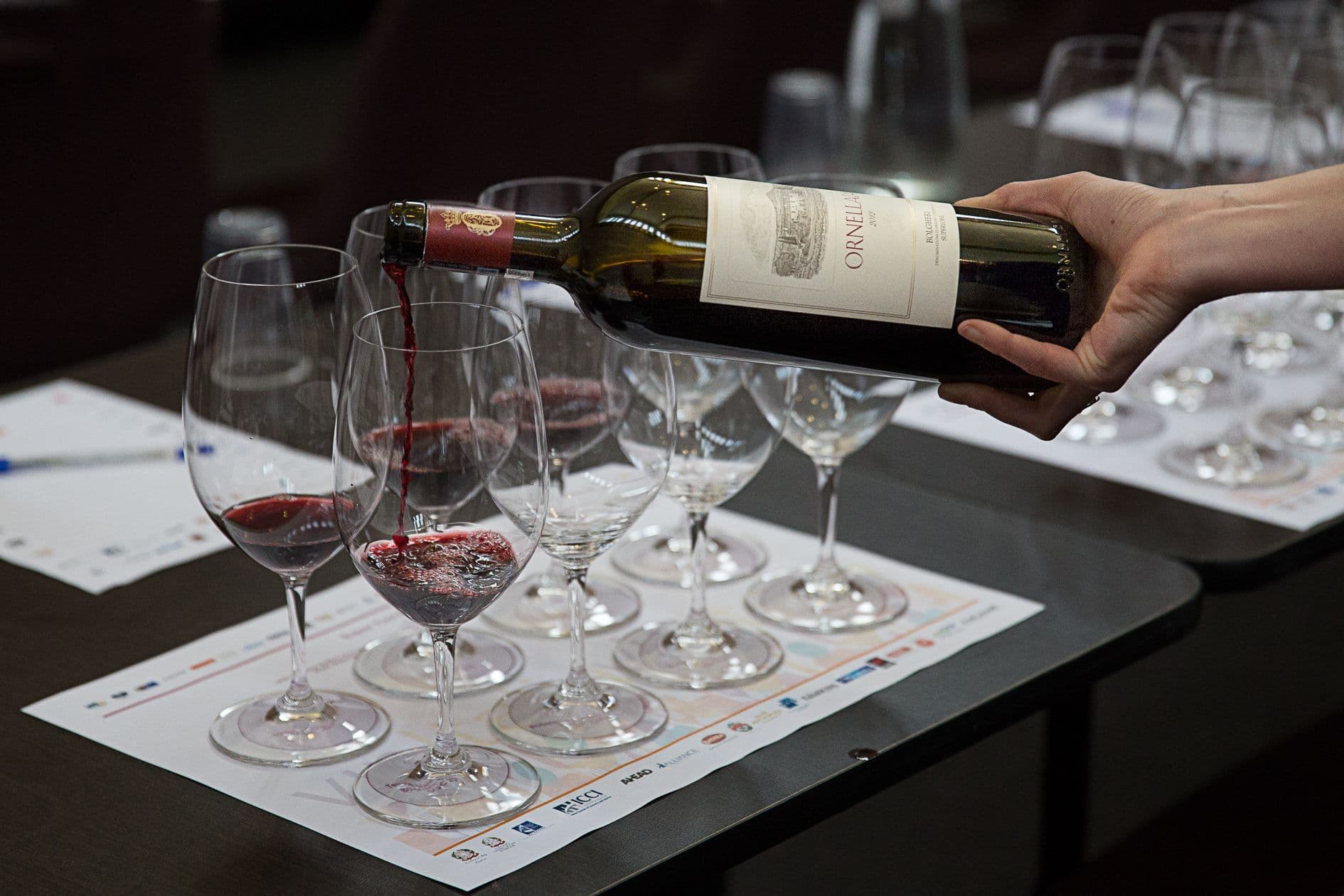 Hand pouring red wine from Ornellaia bottle into tasting glass at wine seminar