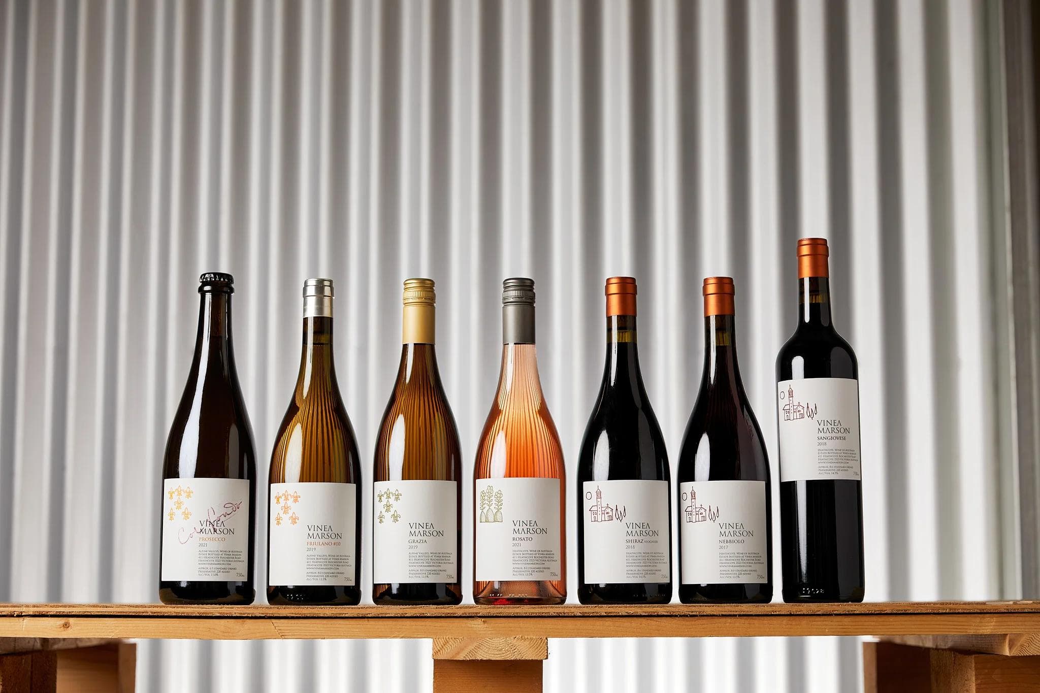 Row of seven Vinea Marson wine bottles on wooden bench