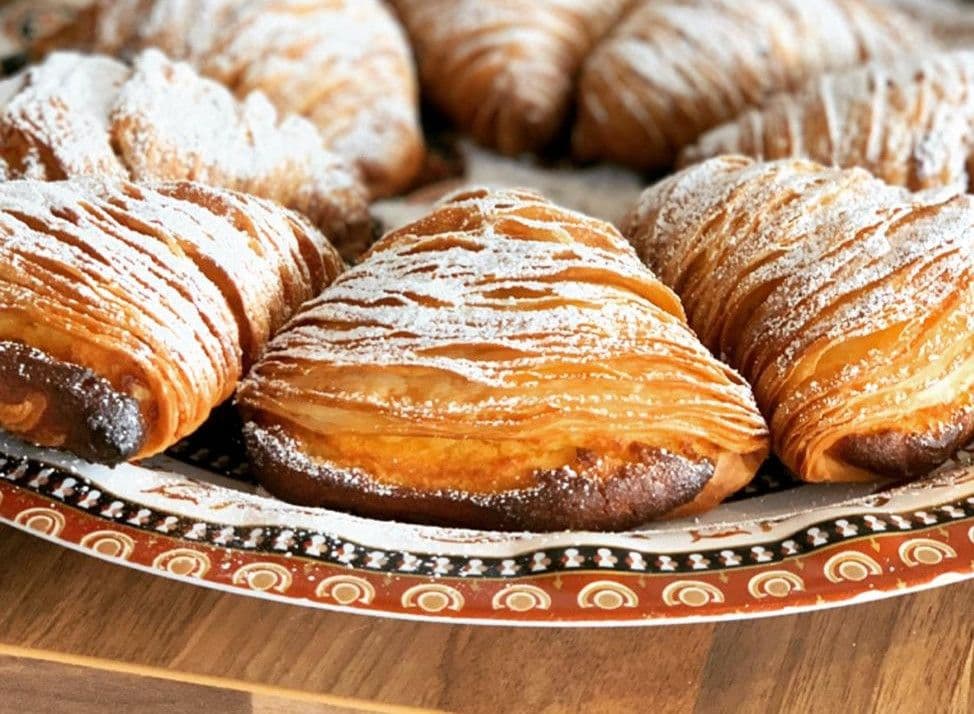 Sfogliatelle pastries dusted with powdered sugar on decorative plate