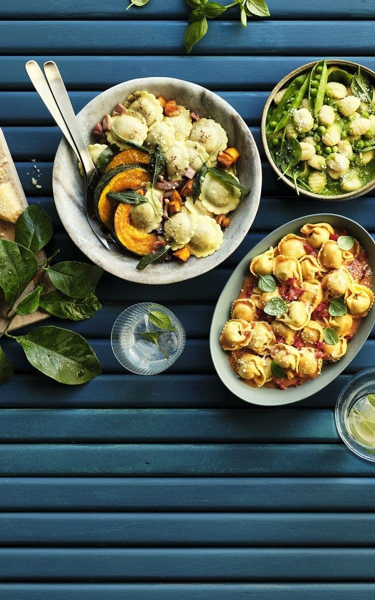Bowls of cooked ravioli, tortellini and gnocchi dishes on blue table