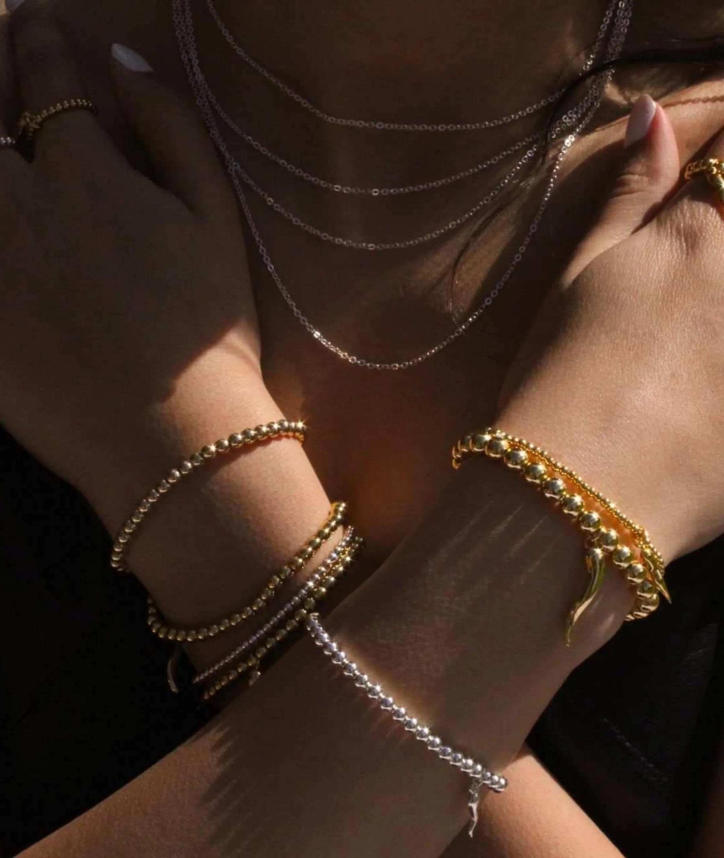 Person wearing layered gold and silver bracelets and necklaces in sunlight
