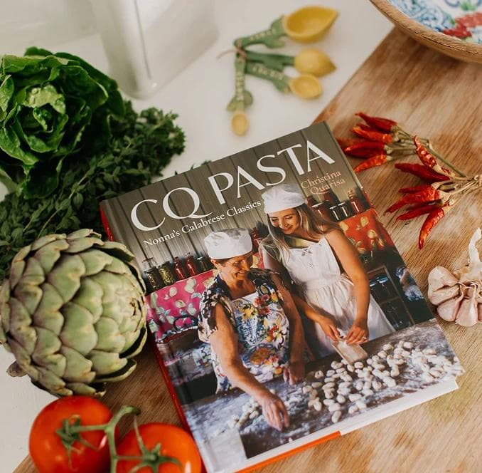 CQ Pasta cookbook surrounded by fresh vegetables and herbs