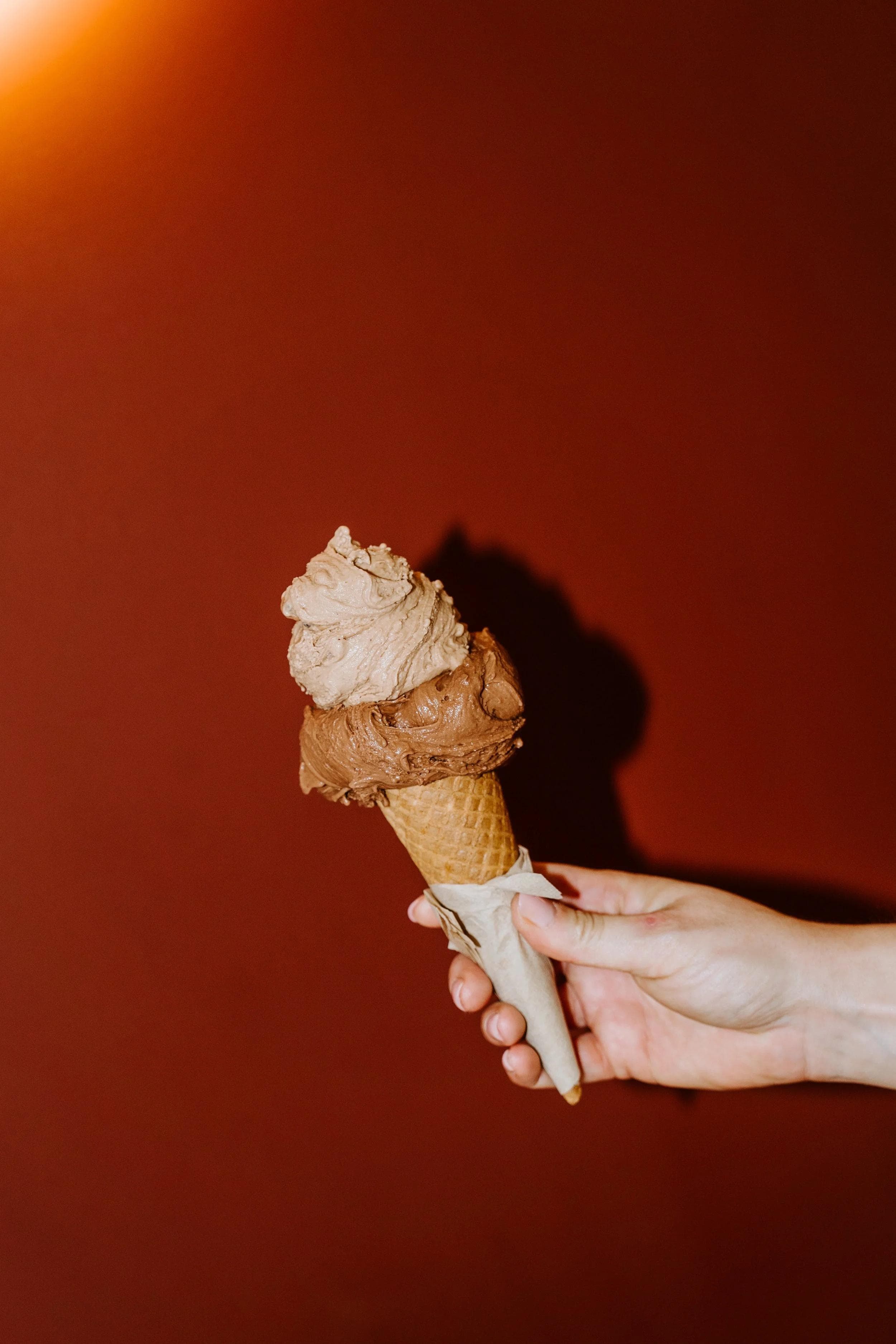 Hand holding chocolate gelato cone against dark red background