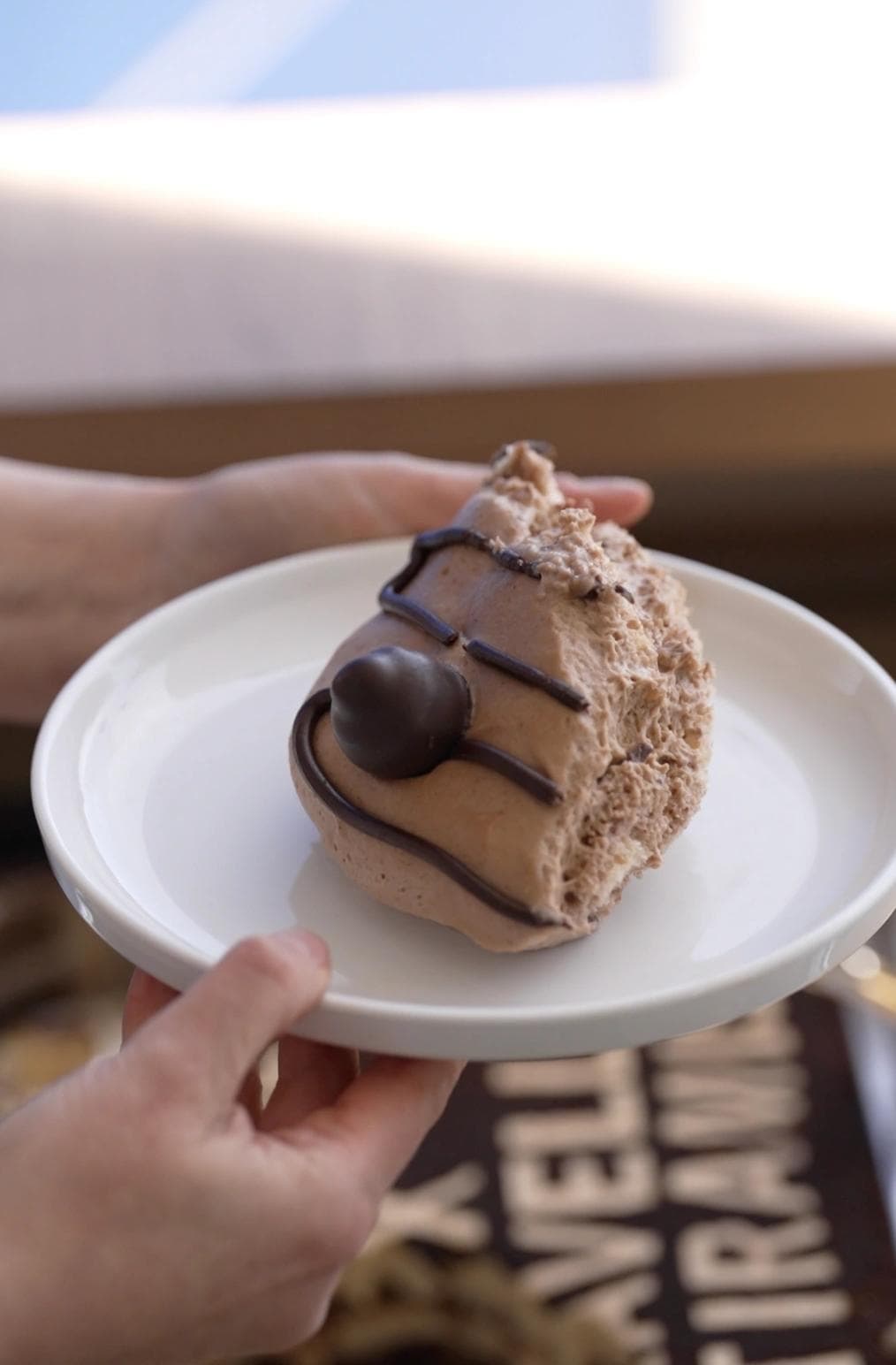 Hand holding plate with chocolate tiramisu topped with chocolate ball