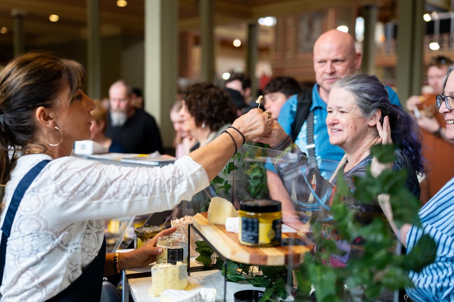 Woman serving cheese samples to smiling festival attendees at an indoor tasting event