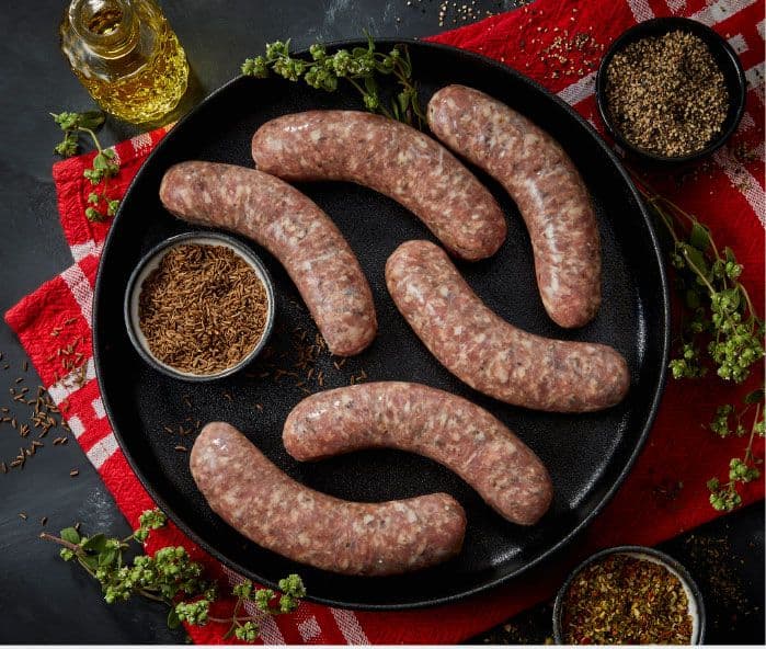 Raw Italian sausages on black plate with herbs and spices