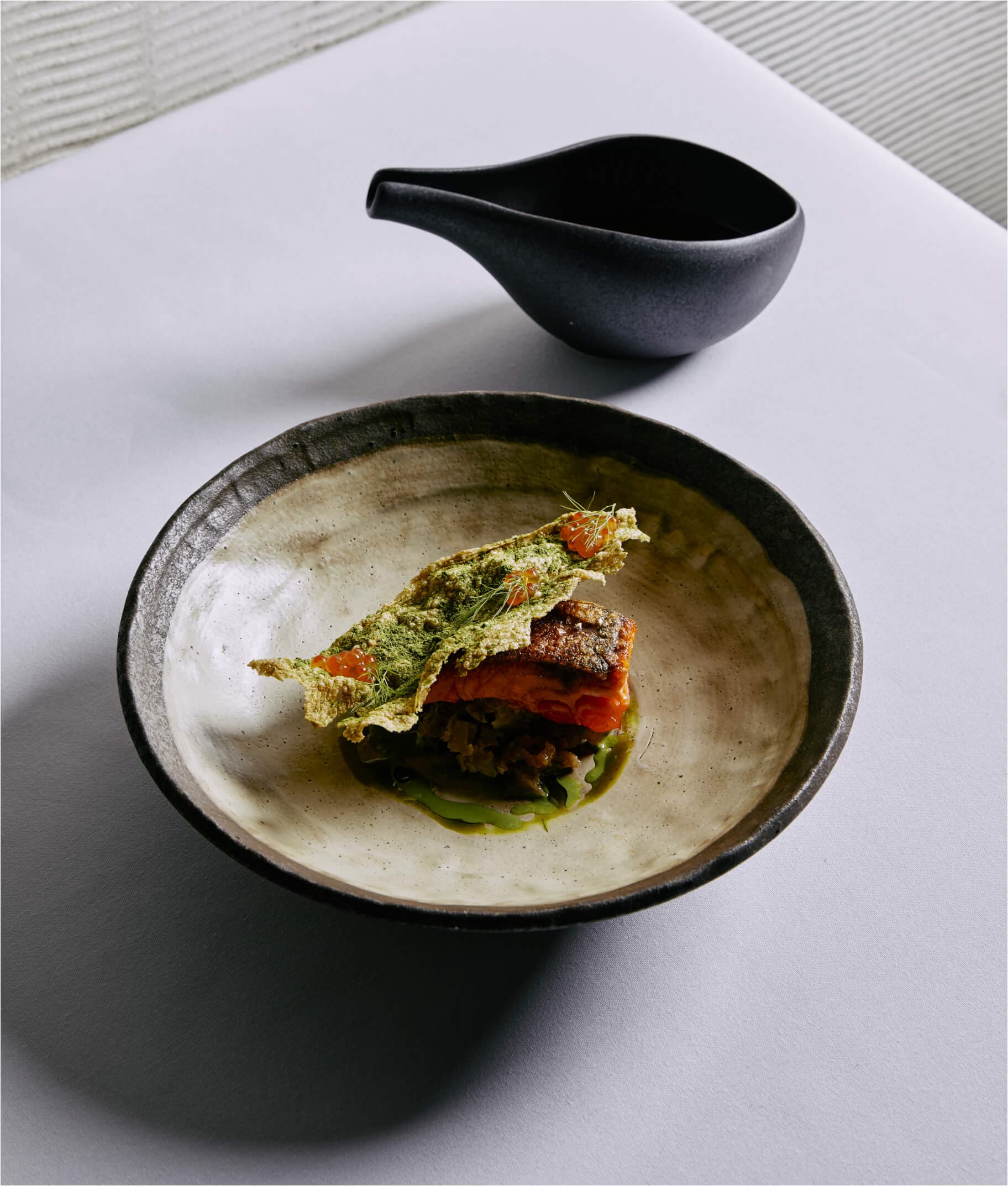 Elegant plated dish with salmon, herb crisp, and dark bowl