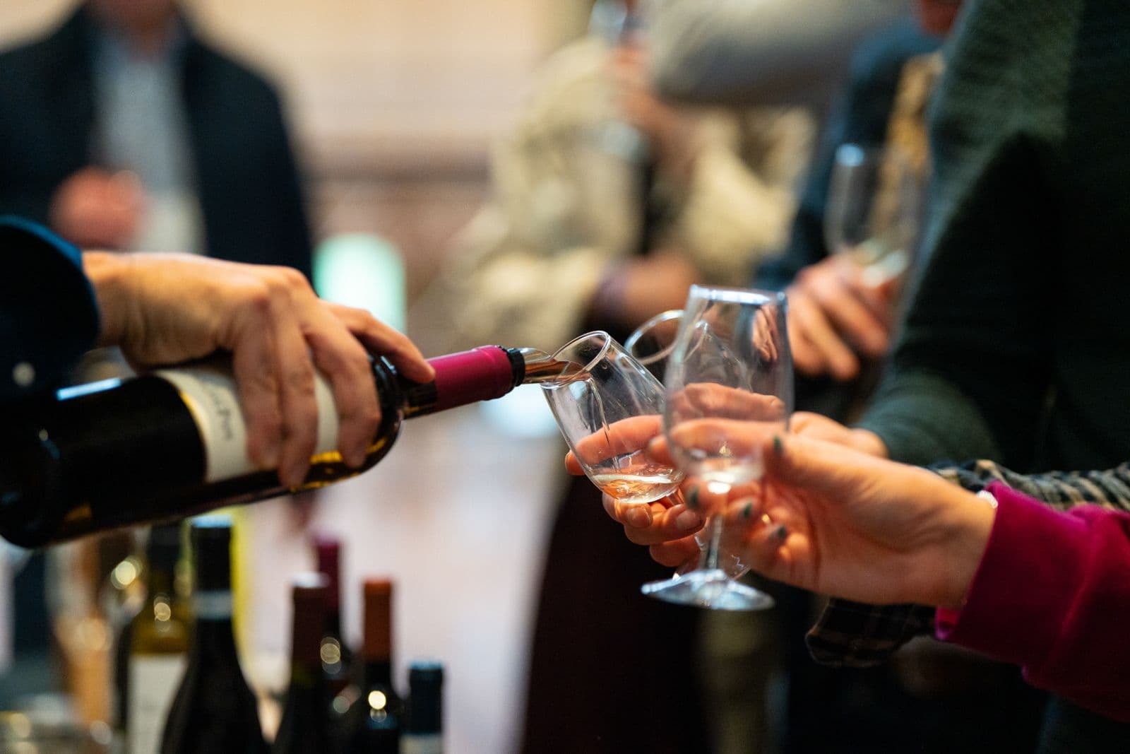 Wine being poured into glasses during a tasting event with attendees