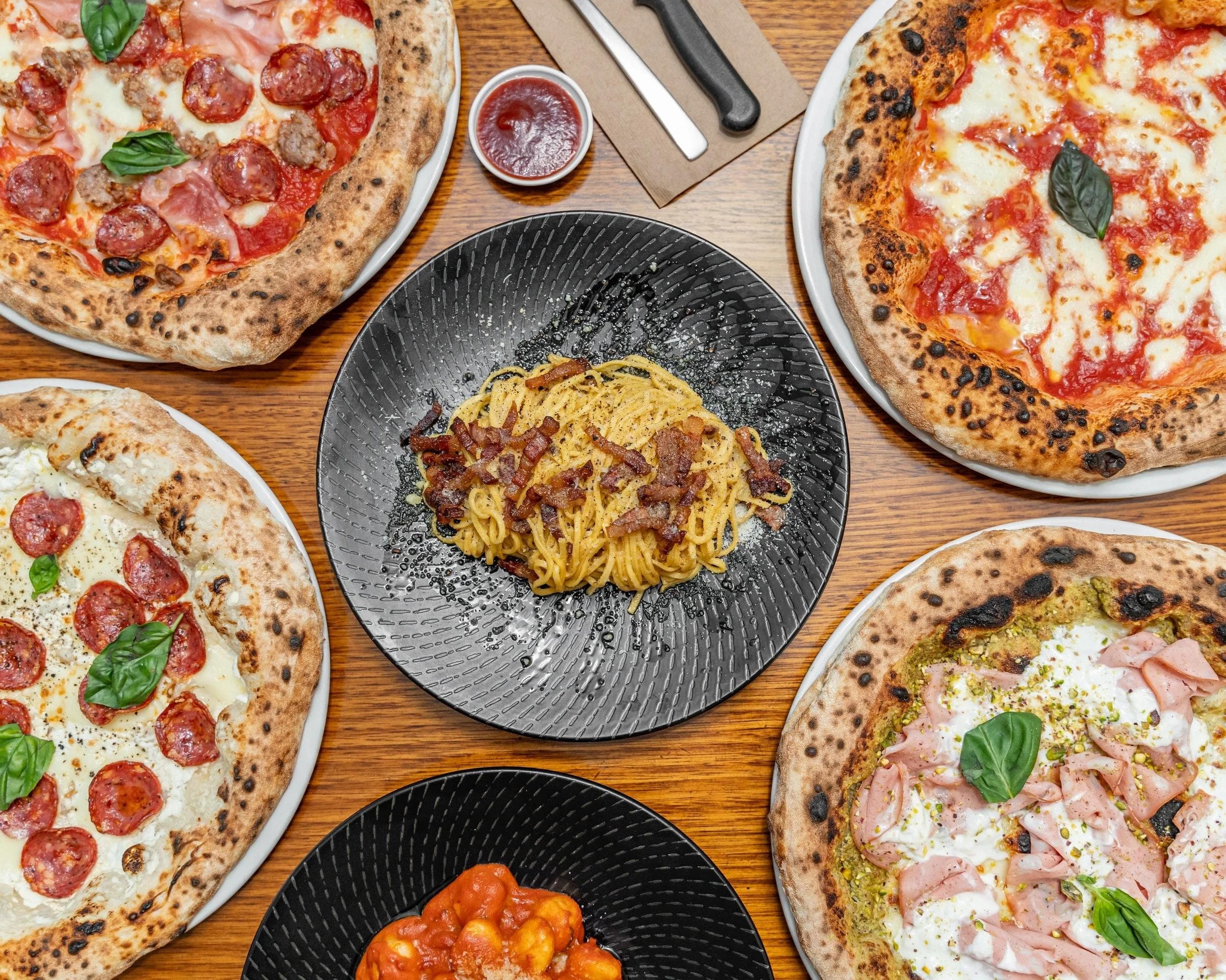 Overhead view of assorted pizzas, spaghetti carbonara and gnocchi on wooden table