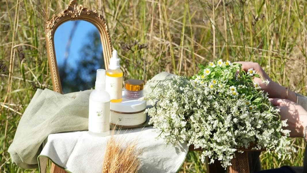 Skincare bottles, mirror and wildflowers styled outdoors in sunlight