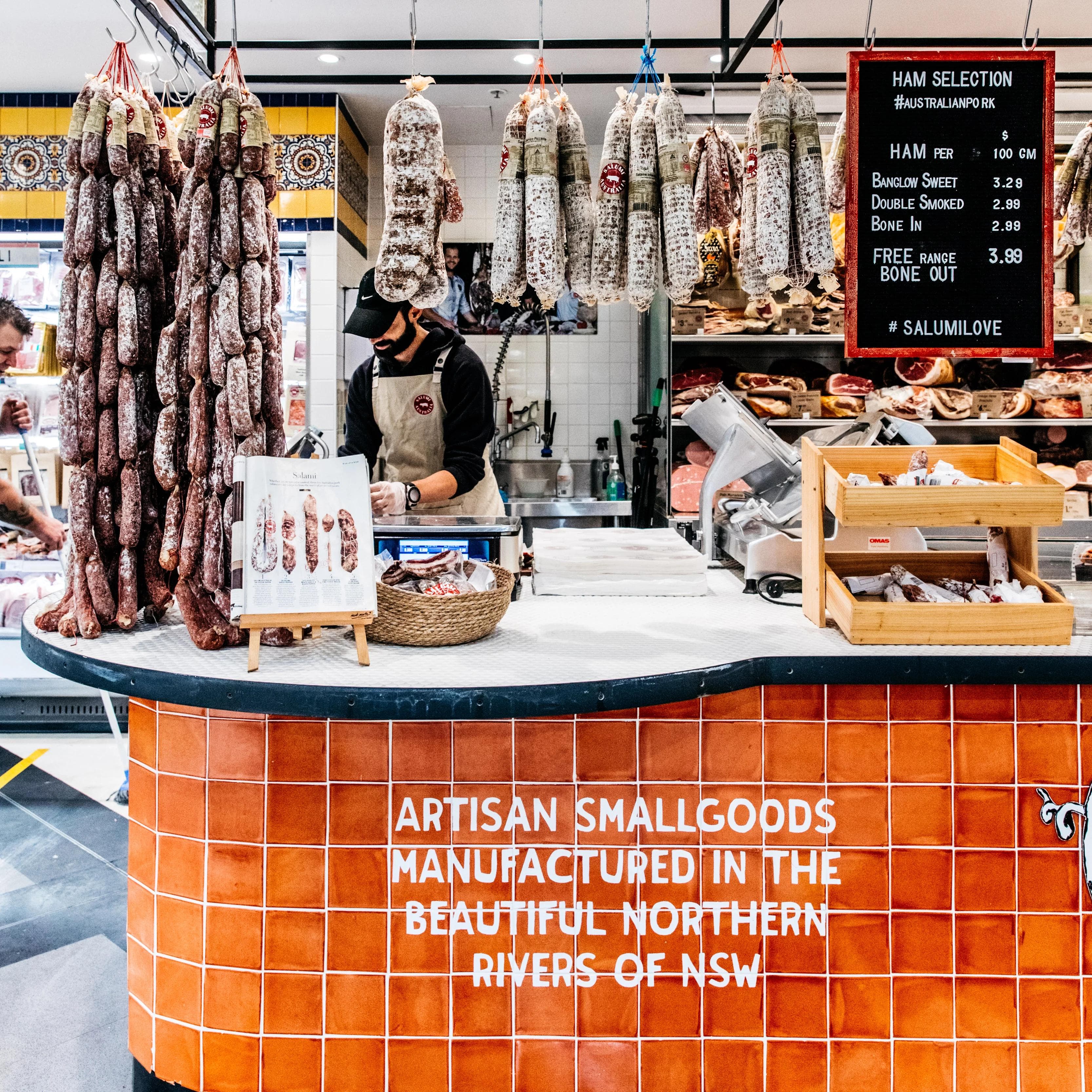 Salumi Australia market stall with hanging salami and staff member