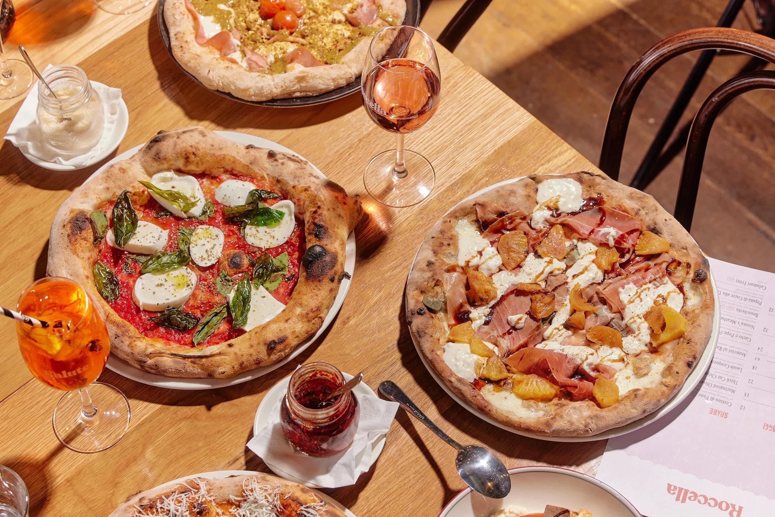 Assorted wood-fired pizzas on wooden table with rosé wine