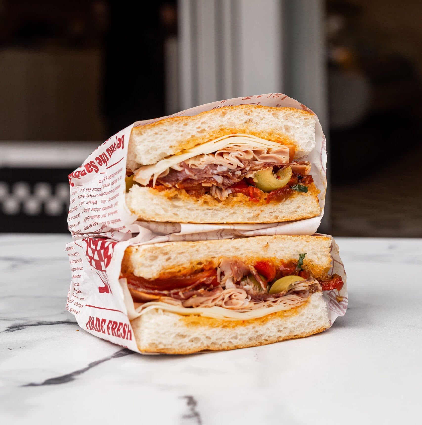 Sandwich stacked halves wrapped in branded paper on marble counter